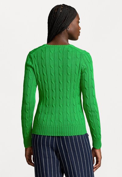 Pull en maille torsadée vert avec des manches longues et un col rond, doté de poignets et d'une base côtelés, associé à un pantalon rayé bleu marine.