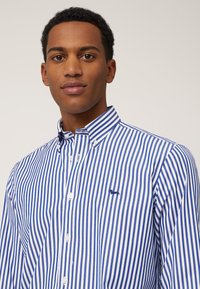 Blauw-wit gestreepte shirt met een button-down kraag, voorzien van een klein geborduurd logo op de borst en witte knopen aan de voorkant.