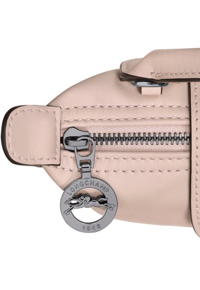 Helles rosa Lederhandtasche mit einem silbernen Metallreißverschluss und einem runden Anhänger mit einem Greyhound-Logo. Glatte Textur mit tonalem Stich.