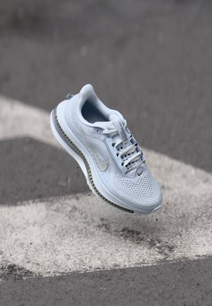 Lyseblå treningssko med mesh-overdel, hvite snørebånd og grå detaljer. Har en dempet såle og en fremtredende swoosh-logo.