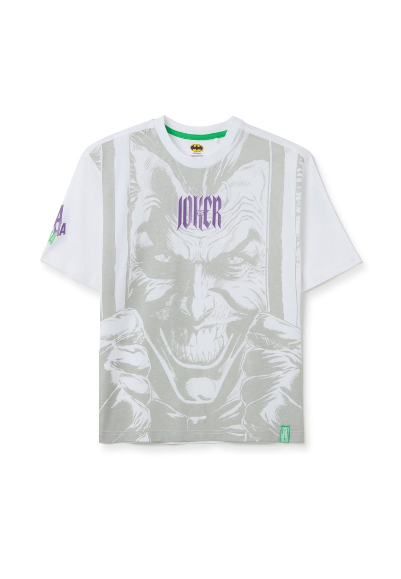 Camiseta blanca de manga corta con un gran gráfico en gris del Joker en la parte frontal. Texto "JOKER" en púrpura sobre la imagen. Etiqueta de marca verde.