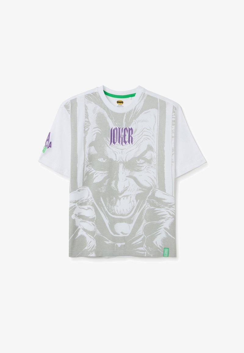 Camiseta blanca de manga corta con un gran gráfico en gris del Joker en la parte frontal. Texto "JOKER" en púrpura sobre la imagen. Etiqueta de marca verde.