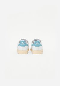 Hvide lædersneakers med en lys blå accent ved hælen, prydet med "Stan Smith"-logoet og en cremet gummisål.