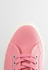 Różowa kanwasowa sneaker z białą gumową podeszwą i różowymi sznurowadłami, przedstawiona z widoku z góry na jednolitym jasnym tle.