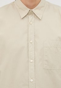 Beige knoopshirt met een klassieke kraag, een borstzak en een zachte, lichte stof. Voorzien van witte knopen en een eenvoudig ontwerp.