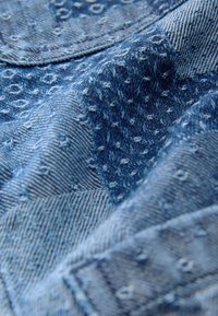 Tessuto di denim blu con motivi goffrati e cuciti e dettagli di cuciture visibili in una vista ravvicinata.