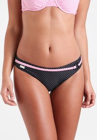 Schwarze Bikiniunterteile mit weißen gepunkteten Mustern, mit einem pinken Akzentstreifen und einem runden Hardware-Detail. Glatte Textur, tief sitzendes Design.
