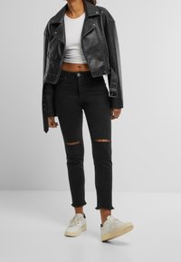 Černá kožená zkrácená biker bunda přes bílý crop top, v kombinaci s černými skinny džíny s roztrhnutými koleny a bílými teniskami.