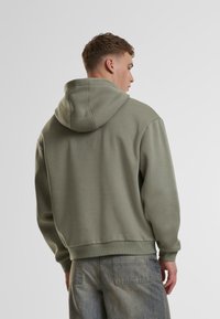 Sudadera verde claro hecha de tejido suave, con capucha ajustable, puños acanalados y un corte relajado, combinada con jeans gris claro.