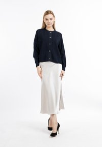 Marineblå strikket cardigan med rund halsudskæring og fem store knapper, parret med en silkeblød beige midiskirt og sorte højhælede sko.