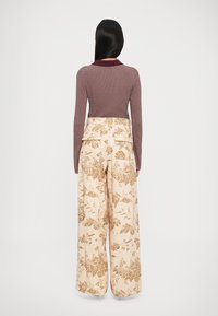 Pulover fucsia cu dungi, cu un guler contrastant, asortat cu pantaloni bej cu croi larg, având un model floral în tonuri de maro.