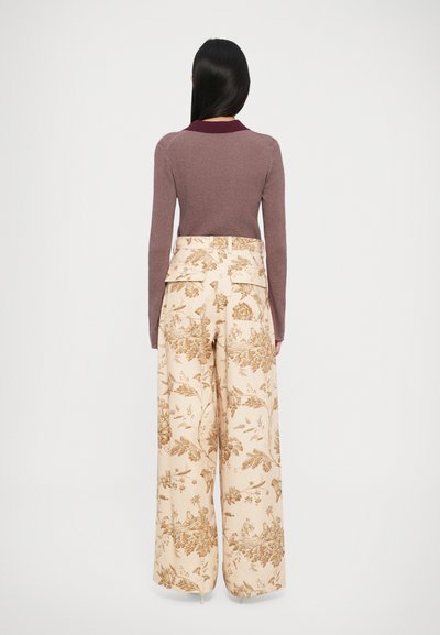 Pull bordeaux côtelé avec un col contrastant, associé à un pantalon beige à jambes larges, arborant un motif floral dans des tons bruns.