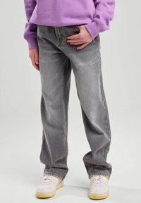 Harmaat farkut, joissa on rento istuvuus, haalistunut pesu, suorat lahkeet ja näkyvät ompeleet. Yhdistetty valkoisten tennareiden ja violetin hupparin kanssa.