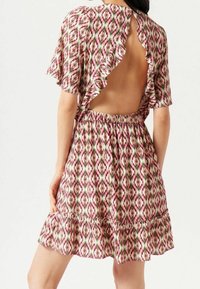 Kortärmad klänning med öppen rygg, prydd med ett flerfärgat geometriskt mönster i rosa, grönt och vitt, samt en volang framtill.