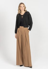 Czarny luźny kardigan z dzianiny z przodem zapinanym na zamek, w połączeniu z beżowymi spodniami o wysokim stanie i szerokich nogawkach, tworzy zdefiniowaną sylwetkę.