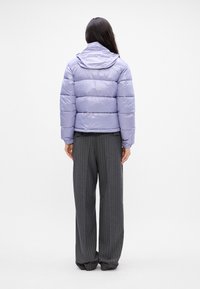 Chaqueta de pluma en un suave lavanda, con capucha y diseño acolchado. Combinada con pantalones de pierna ancha de rayas grises. Tejido suave y brillante.