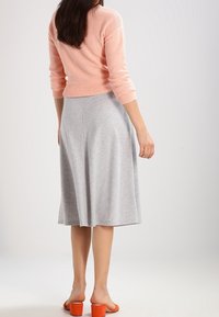 Maglione rosa chiaro a maglia, aderente in vita, abbinato a una gonna svasata grigia, di lunghezza al ginocchio, in tessuto morbido. Sandali con tacco arancioni completano il look.
