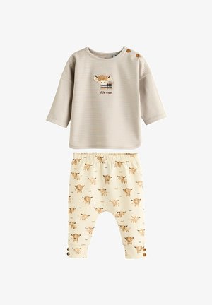 Lichtgrijs gestreept shirt met lange mouwen met een koe graphic, gecombineerd met crèmekleurige broeken met bruine koeienpatronen en knoopaccenten op de mouwen.
