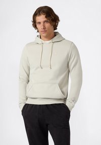Felpa grigia chiaro con cappuccio, tasca anteriore, cordini e logo ricamato. Abbinata a pantaloni jogger neri e testurizzati.