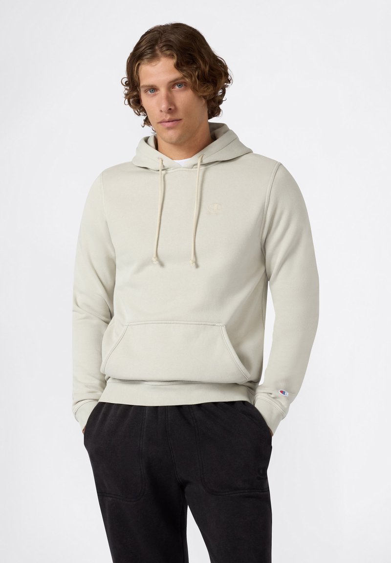 Felpa grigia chiaro con cappuccio, tasca anteriore, cordini e logo ricamato. Abbinata a pantaloni jogger neri e testurizzati.