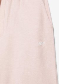 Tissu rose clair texturé avec un petit logo blanc brodé près de la couture, probablement une partie d'un vêtement.