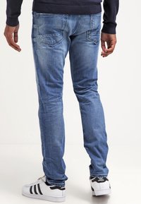 Vaqueros de mezclilla azul con corte slim, textura deslavada y bolsillos traseros. Combinados con zapatillas blancas con rayas negras.