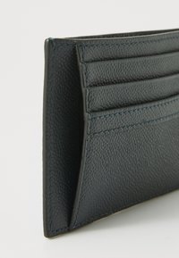 Portafoglio in pelle texturizzata blu scuro con scomparti per carte in verticale e cuciture a contrasto. Presenta un design elegante e sottile, adatto per un facile trasporto.