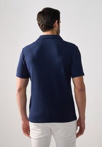 Marineblå ribbet polo skjorte med korte ærmer, med krave og lige kant, kombinert med lyse bukser.