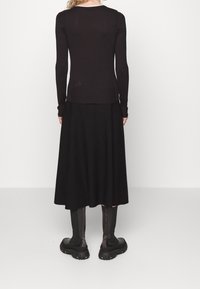 Zwarte langemouwen top met ribbelrand, gecombineerd met een zwarte vloeiende rok en chunky zwarte laarzen. Gladde textuur met een aansluitend ontwerp.