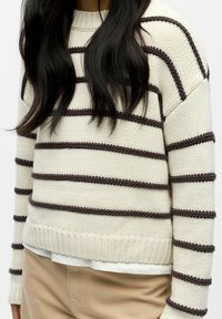 Kremine megzta megztinis su rudomis horizontaliomis juostelėmis, apvalia iškirpte bei borteliais rankogaliais ir apačioje. Dėvimas ant balto marškinio.