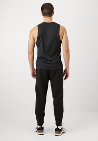 Zwart mouwloos sporttop en zwarte jogpants met structuur, gecombineerd met neutrale sneakers. Schoon ontwerp zonder zichtbare patronen.