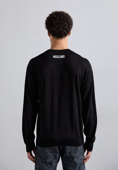 Črn dolg rokav sweatshirt s okroglim izrezom, na hrbtni strani pa je bel logo "MOSCHINO". Tkanina se zdi gladka in mehka.