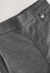 Grauer Stoffbund mit elastischem Rücken und kleinem herzförmigem Metallanhänger, der mit "Clarks" graviert ist und in der Nähe der Seitennaht befestigt ist.