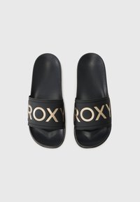 Sandales noires à glissière avec une large sangle ornée du logo doré "ROXY". Texture lisse et bords arrondis, conçues pour le confort et un usage facile.