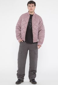 Quilted bomber jacket in pale pink, featuring ribbed cuffs and a zip front. Paired with loose-fitting gray cargo pants and black shoes.
