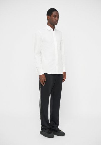 White long-sleeve shirt with a collar, paired with black pants featuring a side stripe. Smooth texture, tailored fit, simple design.