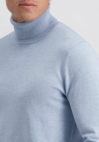 Lichtblauwe coltrui van zachte, gladde stof; strakke pasvorm met ribbelkraag en manchetten; minimale naden zichtbaar op de mouwen.
