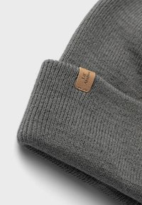Beanie grigia lavorata a maglia con una texture a coste. Presenta un piccolo etichetta in pelle marrone cucita sul risvolto piegato.