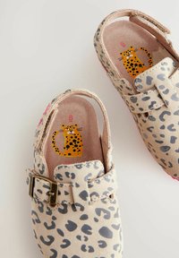 Sabots à imprimé léopard avec un extérieur en suède beige, dotés d'une bride à boucle et d'un design léopard coloré sur la semelle intérieure. Semelles de couleur rose.