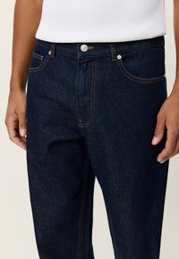 Σκούρα μπλε τζιν με πορτοκαλί ραφές, με μπροστινές τσέπες, κλείσιμο με κουμπί και κλασικό σχέδιο πέντε τσεπών.