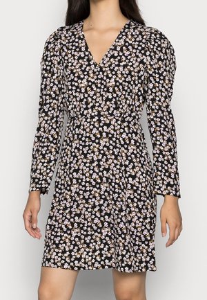 Woman wearing a black dress with long sleeves and a small white and light purple floral pattern, V-neck, and slightly flared skirt.