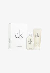Il set regalo Calvin Klein CK One include una bottiglia di plastica bianca e un tubo di crema, entrambi etichettati con testo grigio, confezionati in una scatola bianca.