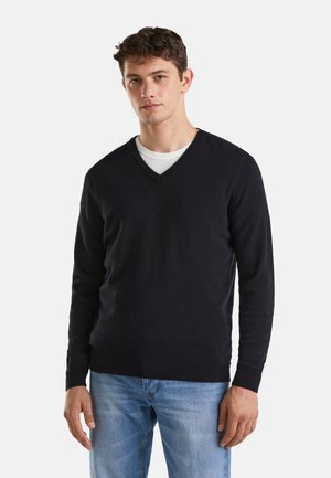 Donkerblauwe v-hals trui van zachte stof met rib gebreide mouwen en zoom, gedragen over een witte ronde hals t-shirt, gecombineerd met lichtblauwe jeans.