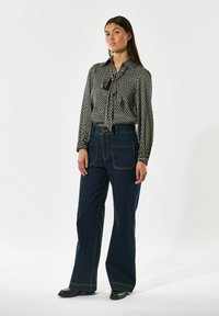 Svartvit mönstrad blus med en knytning vid halsen, kombinerad med högmidjade mörkblå vida jeans. Båda har kontrasterande sömmar.