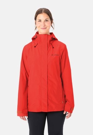 Donna che indossa una giacca impermeabile rossa con cappuccio, cerniera frontale e polsini con Velcro, in piedi e sorridente su uno sfondo uniforme.