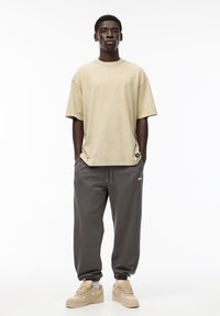 Beige oversized T-shirt med korte ærmer, grå sweatpants med elastiske manchetter og cremefarvede sneakers. Simpelt design uden fremtrædende mønstre.