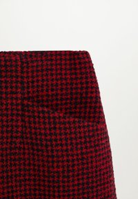 Tessuto a motivo houndstooth rosso e nero, con una finitura testurizzata. In evidenza la trama del tessuto e il profilo dell'indumento.