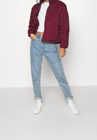 Burgunderfärgad puffjacka med en kort design, ihopparad med ljusblå högmidjade jeans och vita sneakers. Enkelt, texturerat tyg.