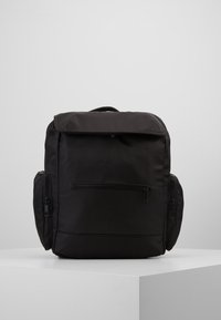 Mochila negra con un acabado de tela suave, dos bolsillos laterales con cremallera y un gran compartimento superior. Cuenta con un asa superior y correas ajustables.