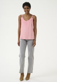 Roza srajčka s čipkastim detajlom na vratu, v kombinaciji s svetlo sivo visokim jeansom in svetlim gležnjarjem. Gladka tekstura tkanine.